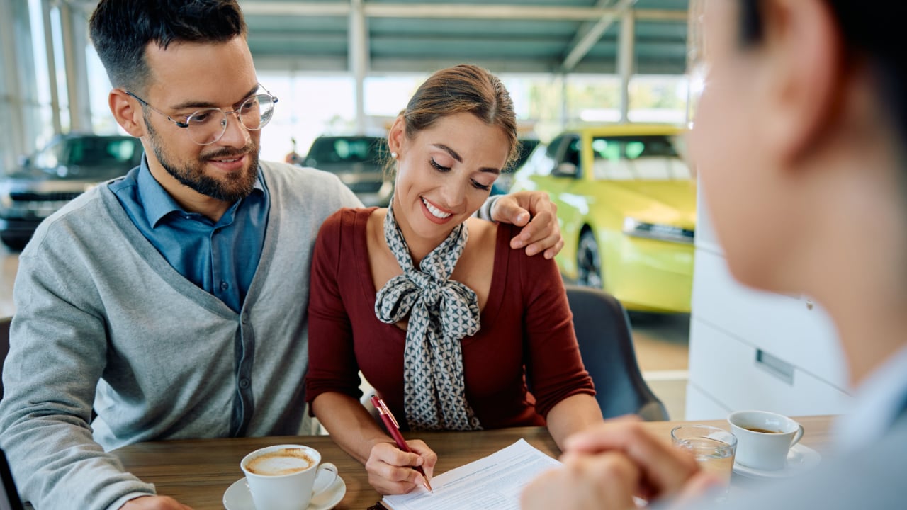 couple en train de signer un contrat de financement pour un nouveau véhicule