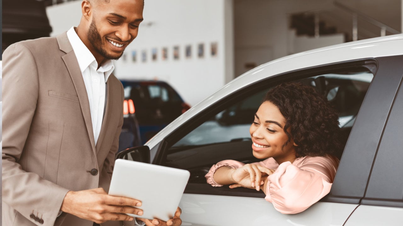 young woman in a car discussing with a sales representative at a dealership