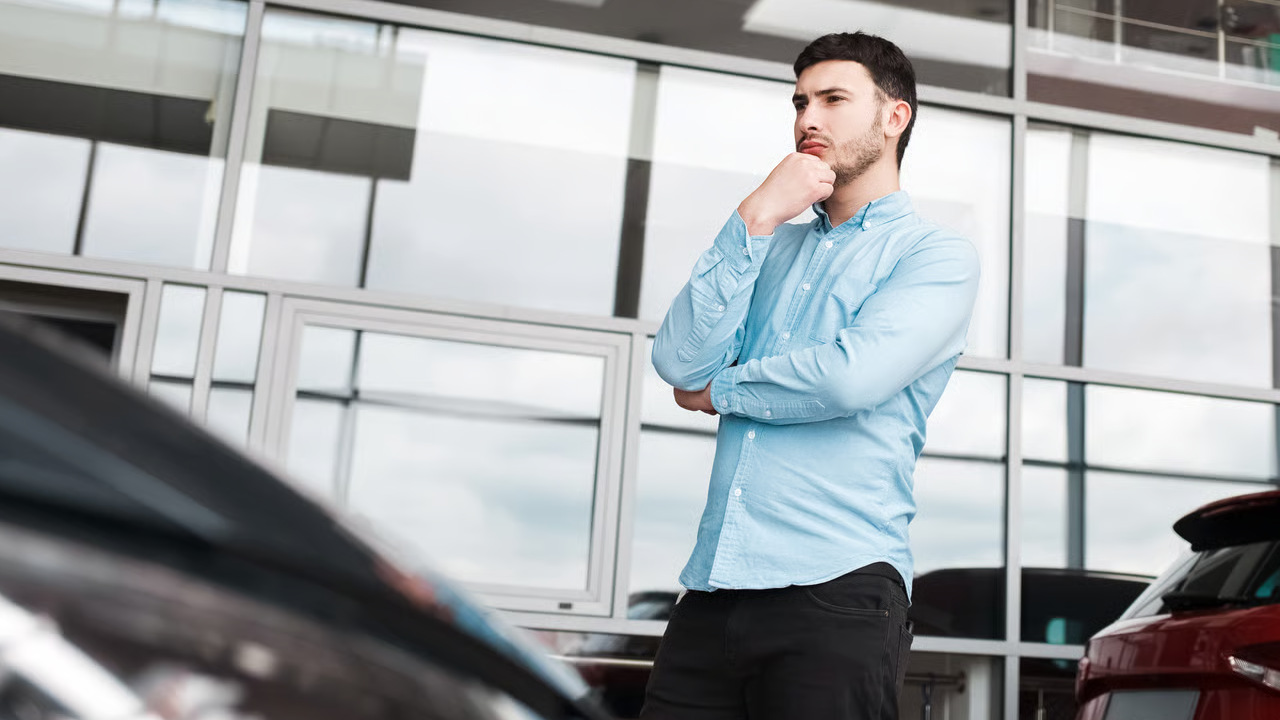 Un homme pensif regarde des voitures chez un concessionnaire automobile