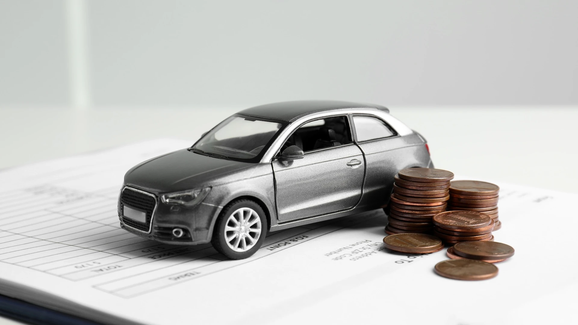 Miniature car and stacks of coins on documents, illustrating the preparation of an auto financing application for second- or third-chance credit.