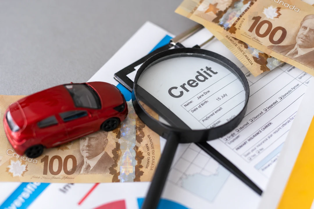 Magnifying glass over a credit document, with a miniature car and Canadian banknotes, illustrating the preparation of an auto financing application.