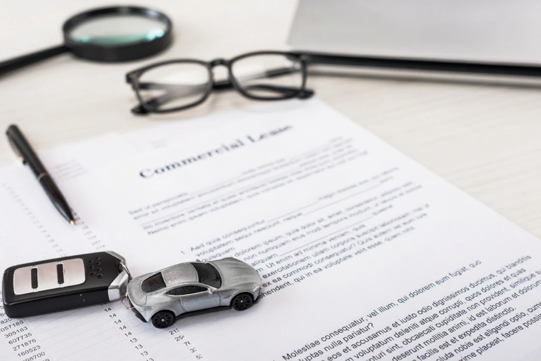 Miniature car, key and glasses resting on documents for an auto loan application.