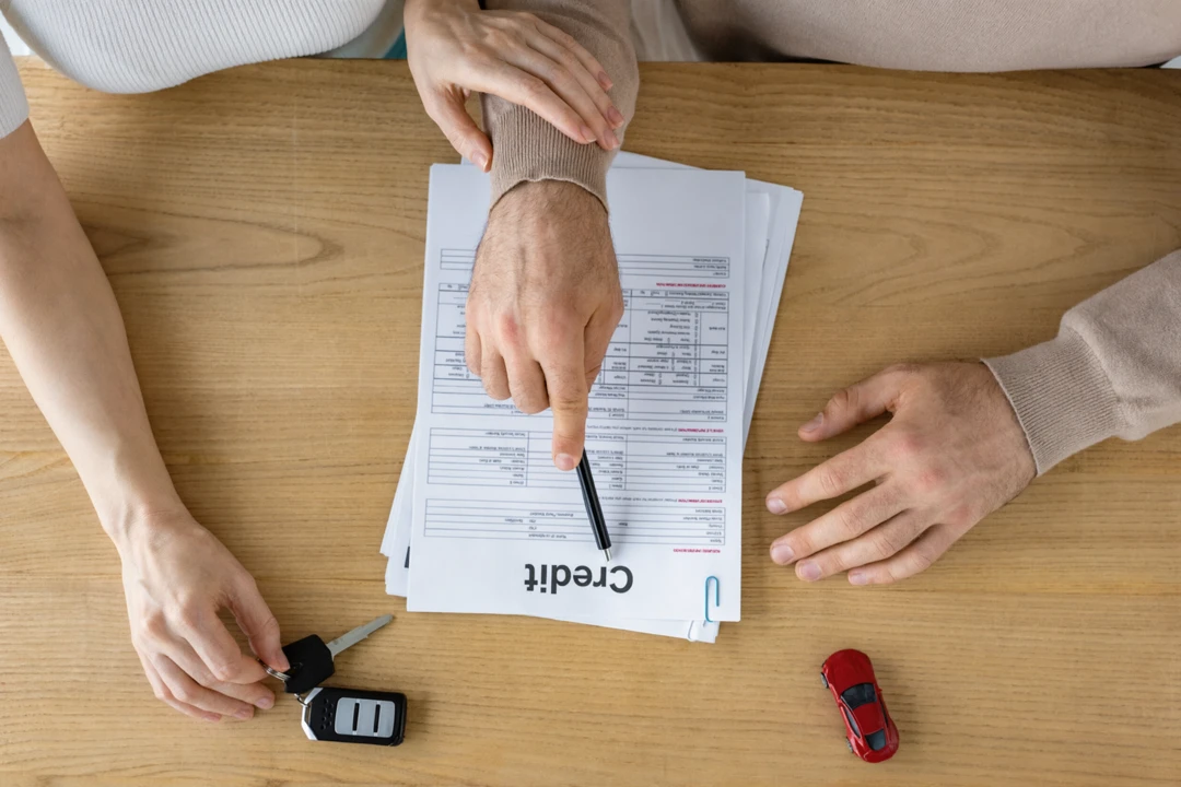 Two people reviewing credit documents on a table with a car key for second- or third-chance auto financing.