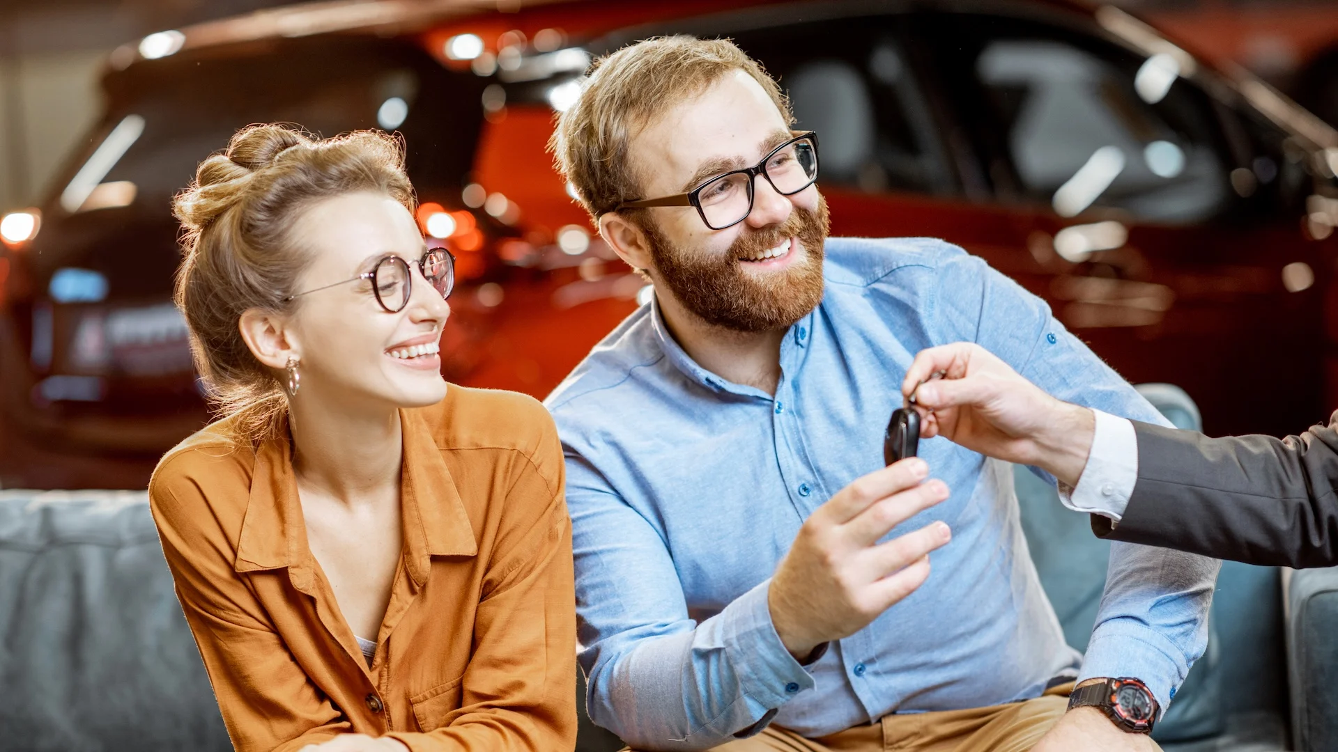 Couple receiving a car key at a dealership, illustrating the choice between leasing and second-chance auto financing.