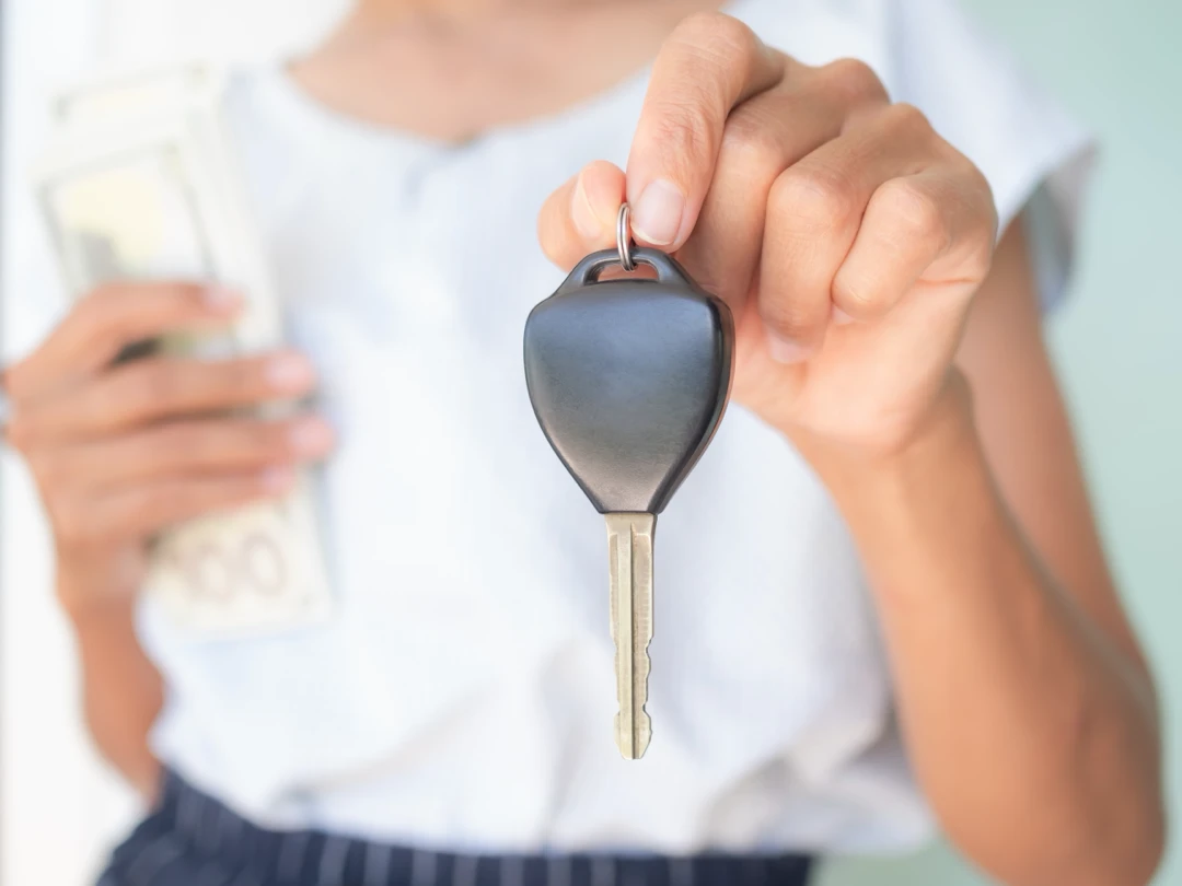 Person holding a car key and banknotes, illustrating vehicle ownership through auto financing.