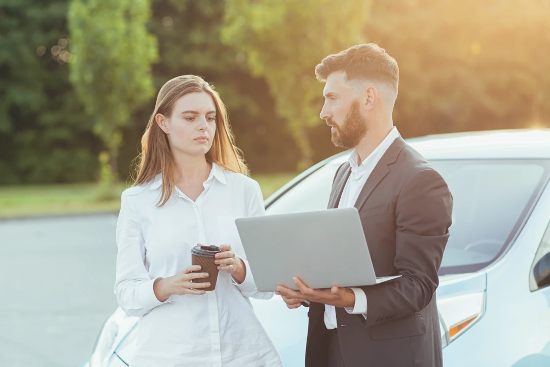 Advisor showing a customer information on a laptop beside a car to compare the total cost of leasing and financing.
