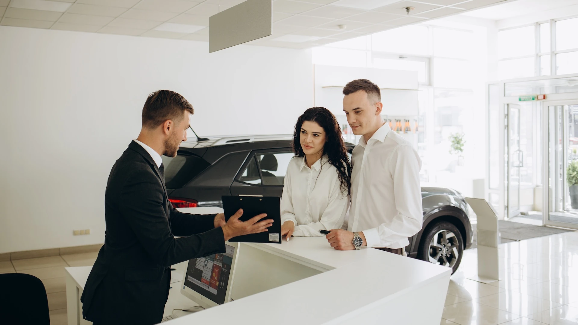 Auto financing advisor presenting loan options to a couple at a car dealership.