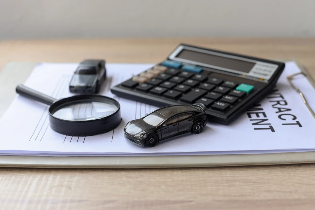 Calculator, magnifying glass and car key on documents, illustrating the comparison of multiple auto financing offers.