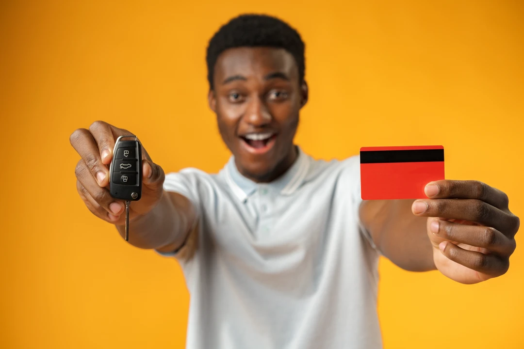 Young man holding a car key and bank card, illustrating a first vehicle purchase.