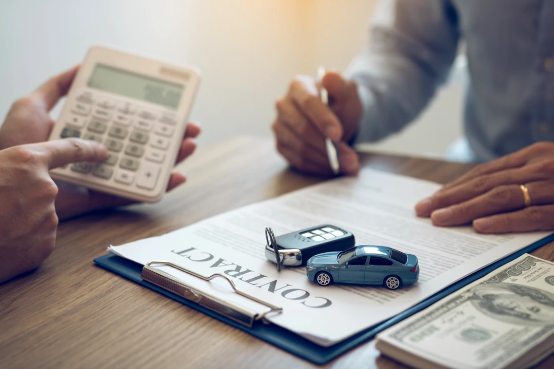 Car financing contract, calculator and miniature vehicle illustrating loan amounts and down payments.