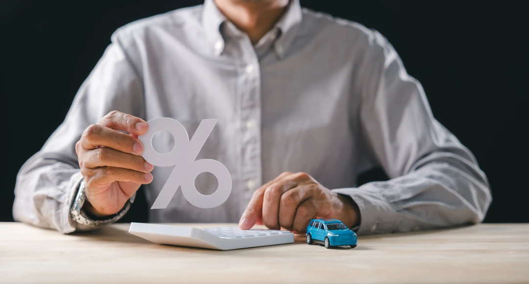 Man holding a percentage symbol near a miniature car, illustrating the assessment of an auto loan.