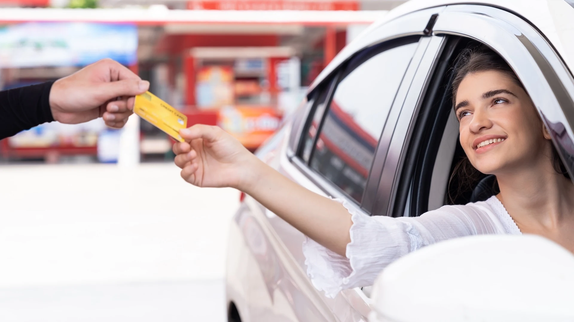 Woman behind the wheel holding out a bank card to make a payment related to her vehicle.