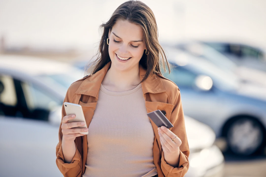Woman checking her phone while holding a bank card, illustrating the reduction of credit card balances before an auto loan.